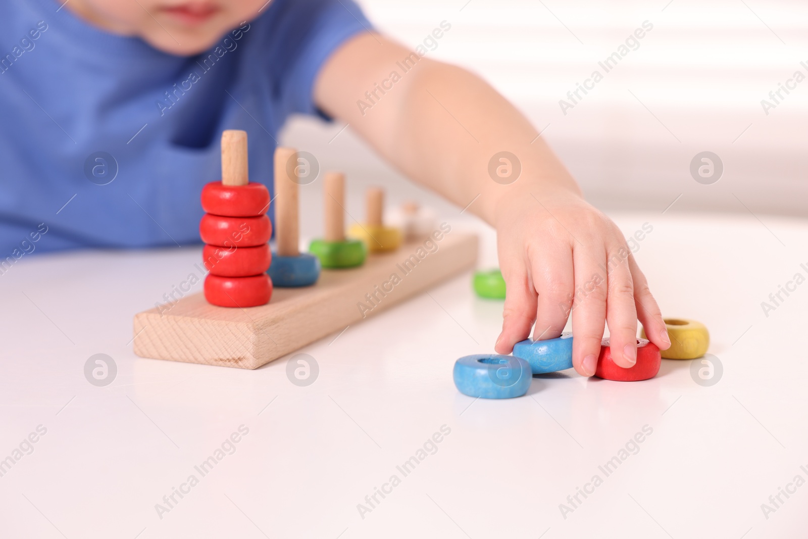 Photo of Motor skills development. Little boy playing with stacking toy at white table indoors, closeup