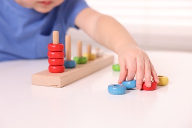 Motor skills development. Little boy playing with stacking toy at white table indoors, closeup