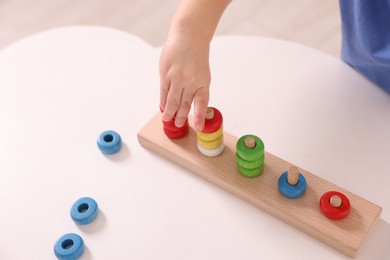 Photo of Motor skills development. Little boy playing with stacking toy at white table indoors, closeup