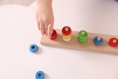 Motor skills development. Little boy playing with stacking toy at white table indoors, closeup