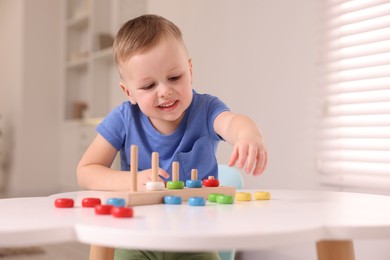 Photo of Motor skills development. Little boy playing with stacking toy at white table indoors