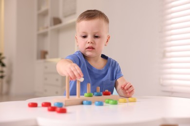 Motor skills development. Little boy playing with stacking toy at white table indoors