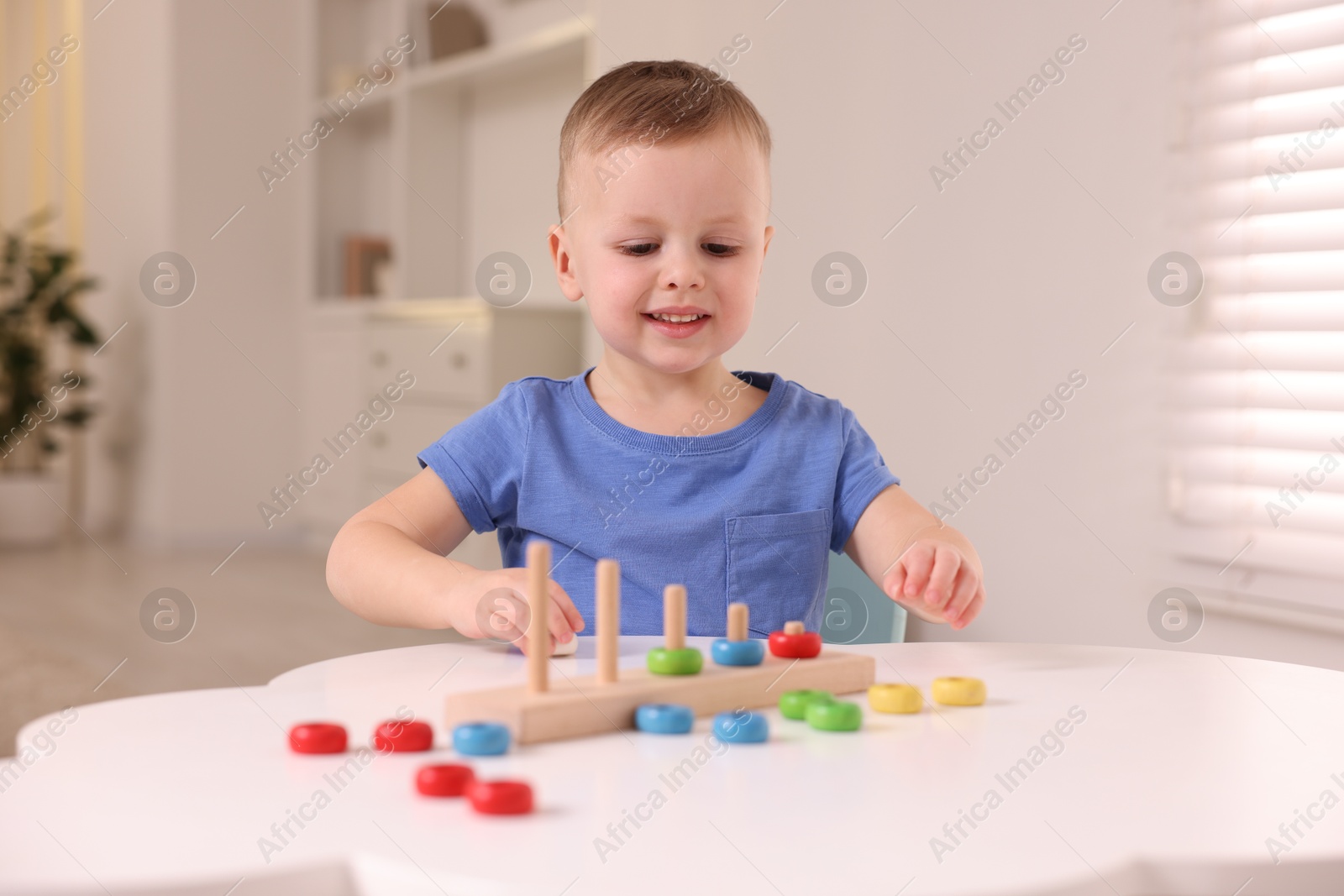 Photo of Motor skills development. Little boy playing with stacking toy at white table indoors