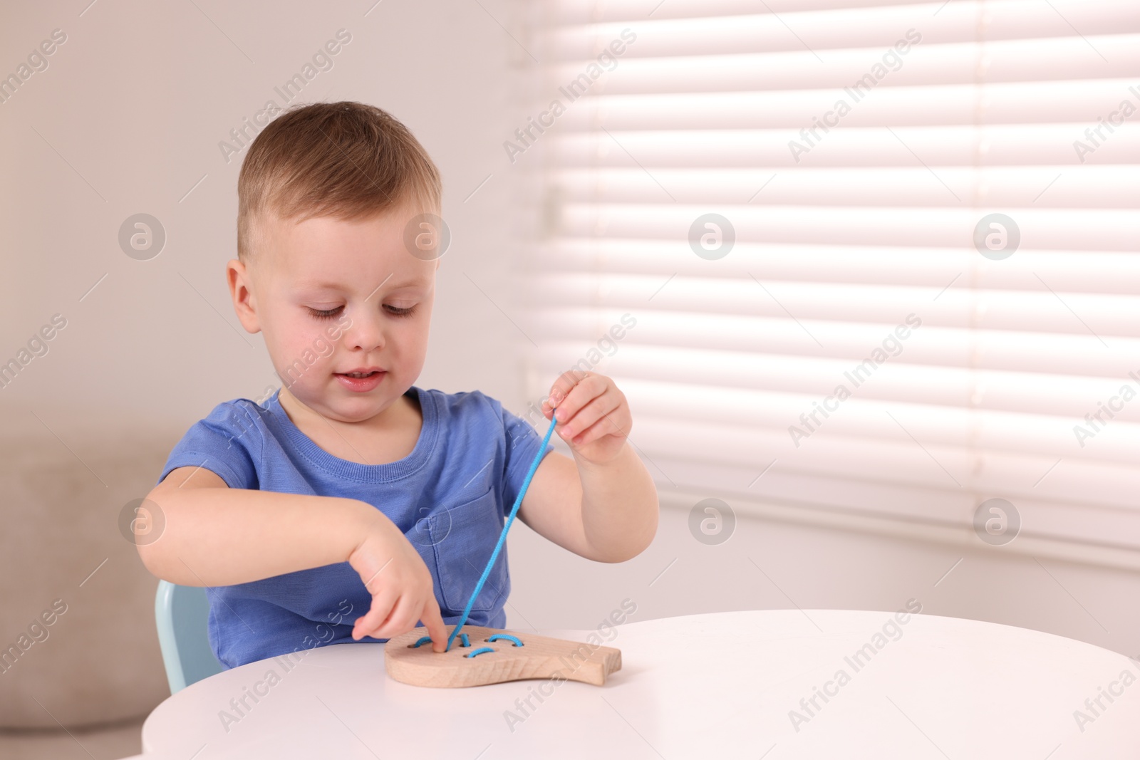 Photo of Motor skills development. Little boy playing with lacing toy at white table indoors, space for text