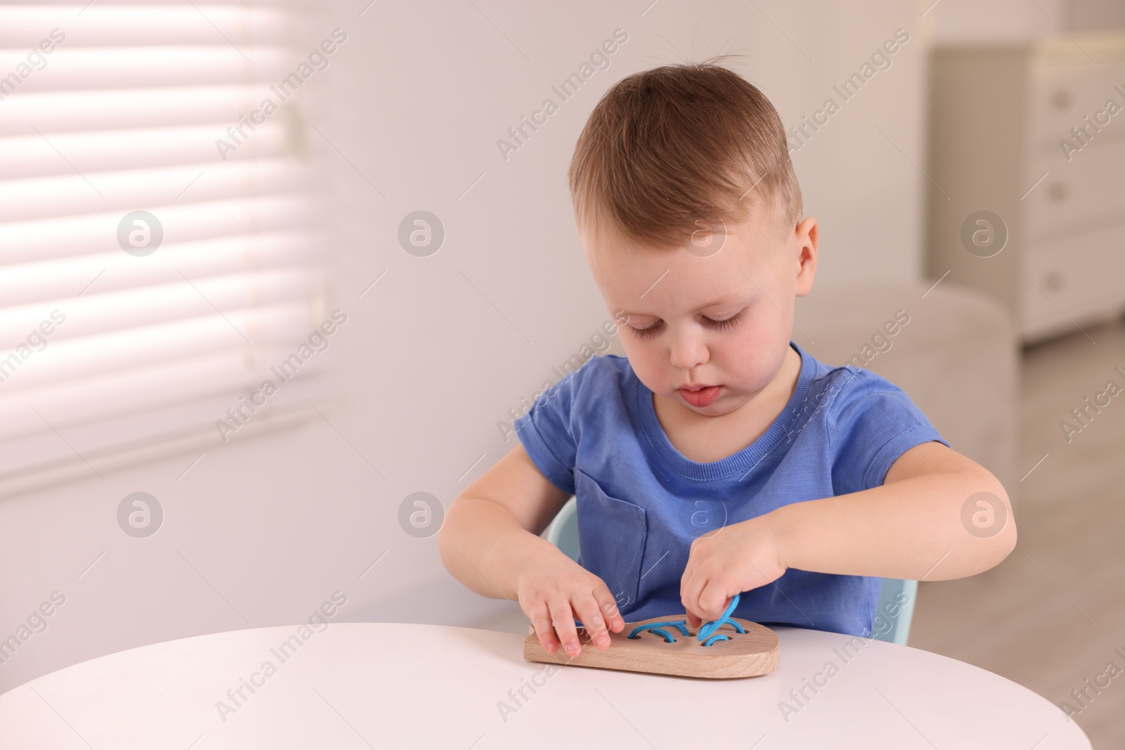 Photo of Motor skills development. Little boy playing with lacing toy at white table indoors, space for text