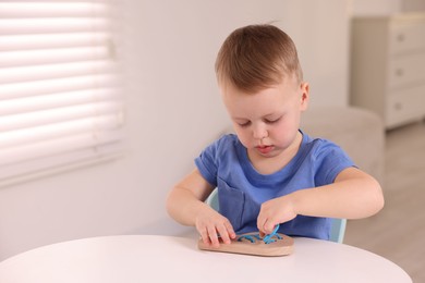 Motor skills development. Little boy playing with lacing toy at white table indoors, space for text