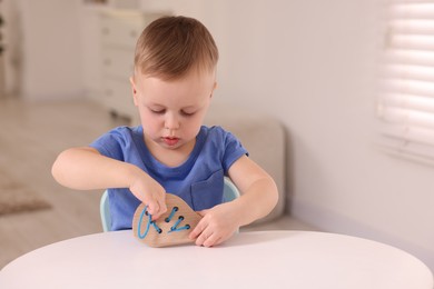 Motor skills development. Little boy playing with lacing toy at white table indoors, space for text