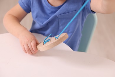 Motor skills development. Little boy playing with lacing toy at white table indoors, closeup