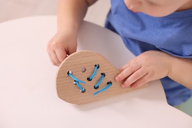 Photo of Motor skills development. Little boy playing with lacing toy at white table indoors, closeup