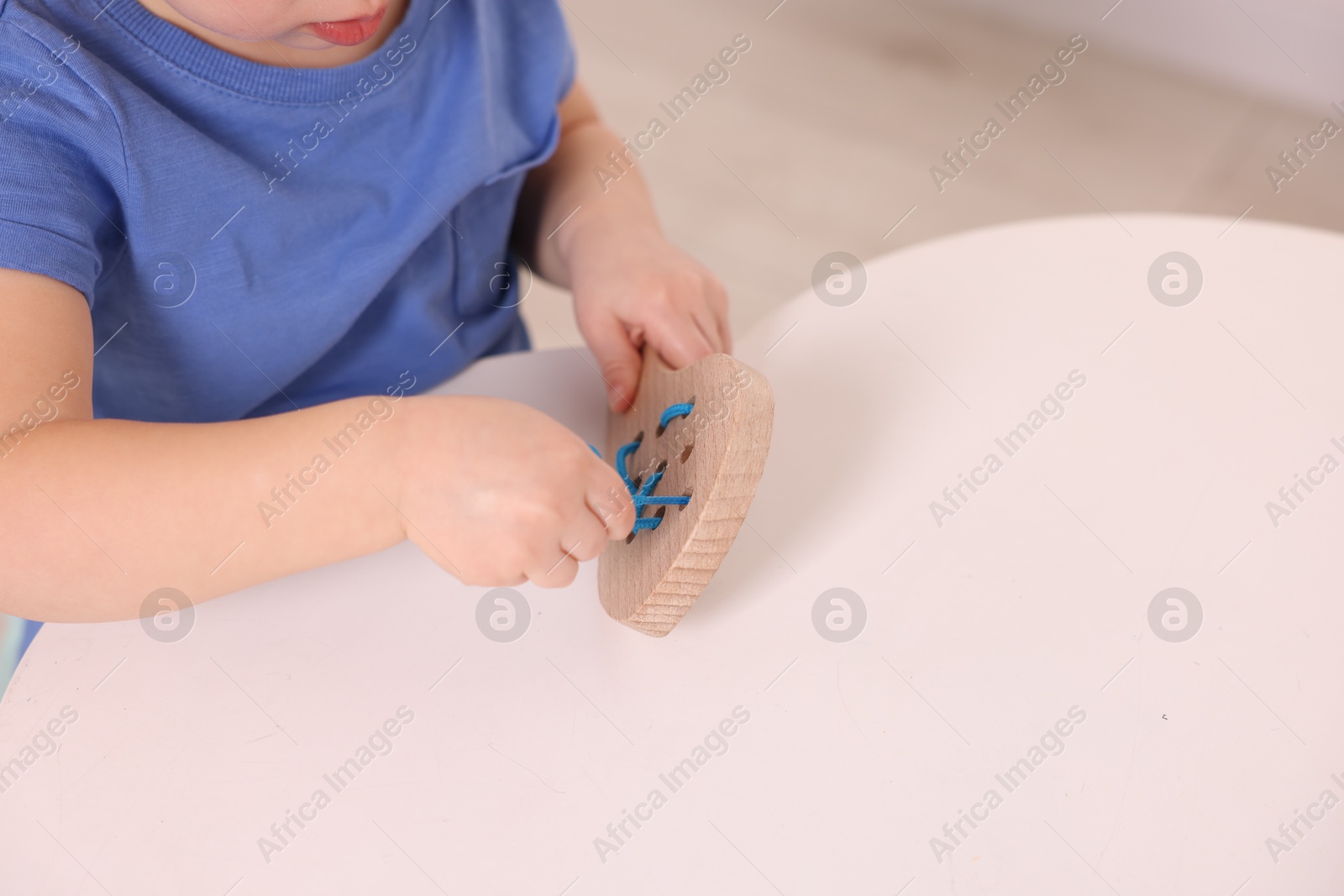 Photo of Motor skills development. Little boy playing with lacing toy at white table indoors, closeup. Space for text