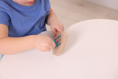 Motor skills development. Little boy playing with lacing toy at white table indoors, closeup. Space for text