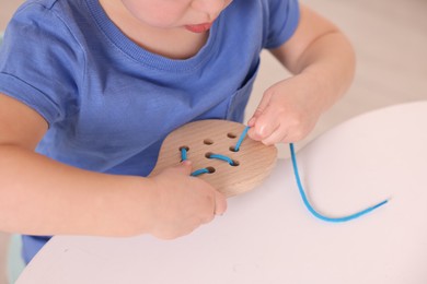 Motor skills development. Little boy playing with lacing toy at white table indoors, closeup