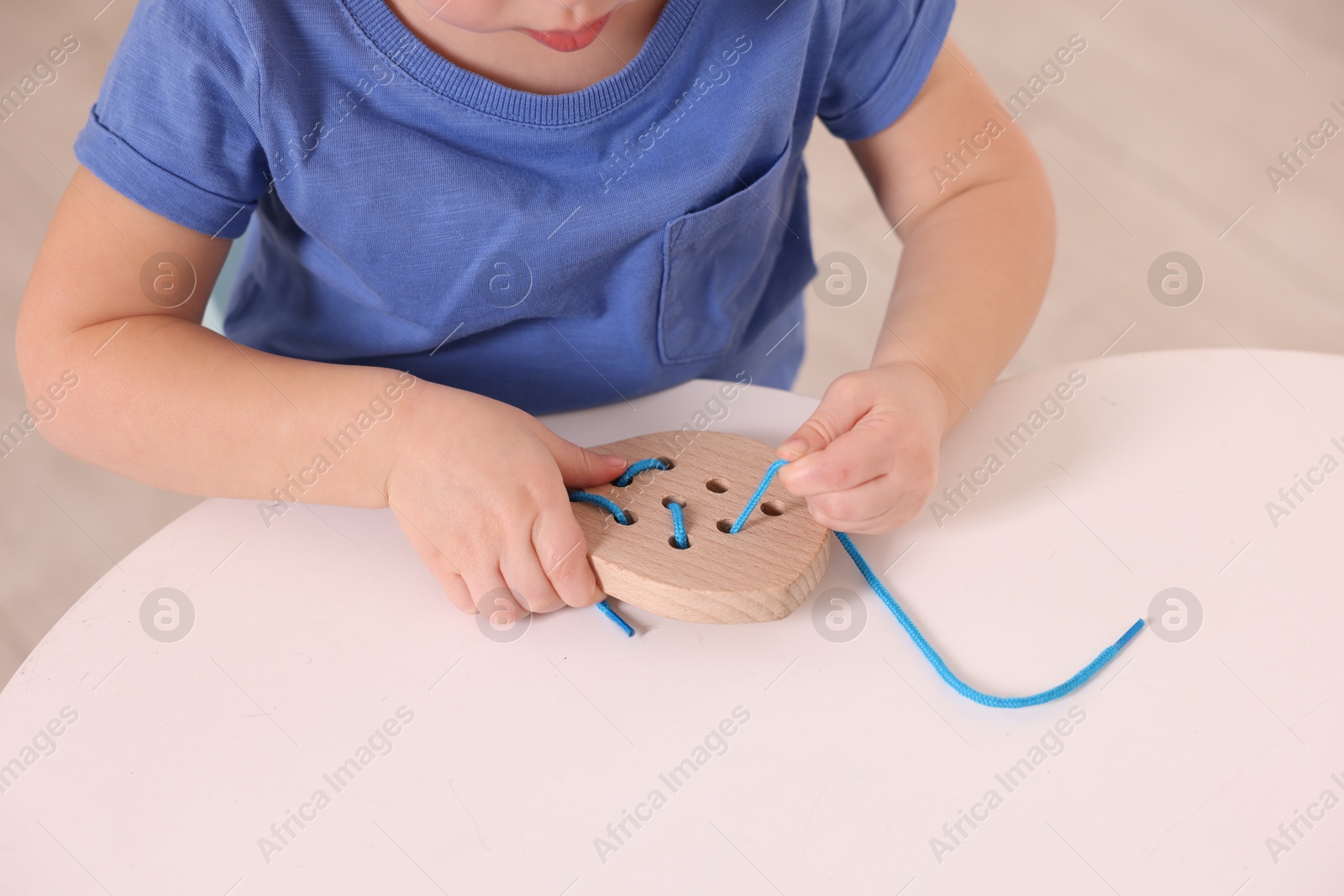 Photo of Motor skills development. Little boy playing with lacing toy at white table indoors, closeup