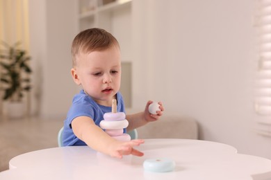 Photo of Motor skills development. Little boy playing with stacking toy at white table indoors, space for text