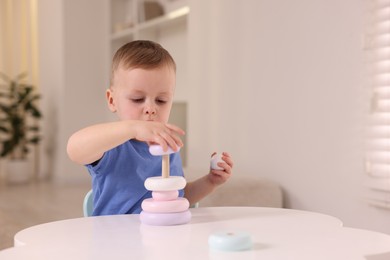 Motor skills development. Little boy playing with stacking toy at white table indoors, space for text