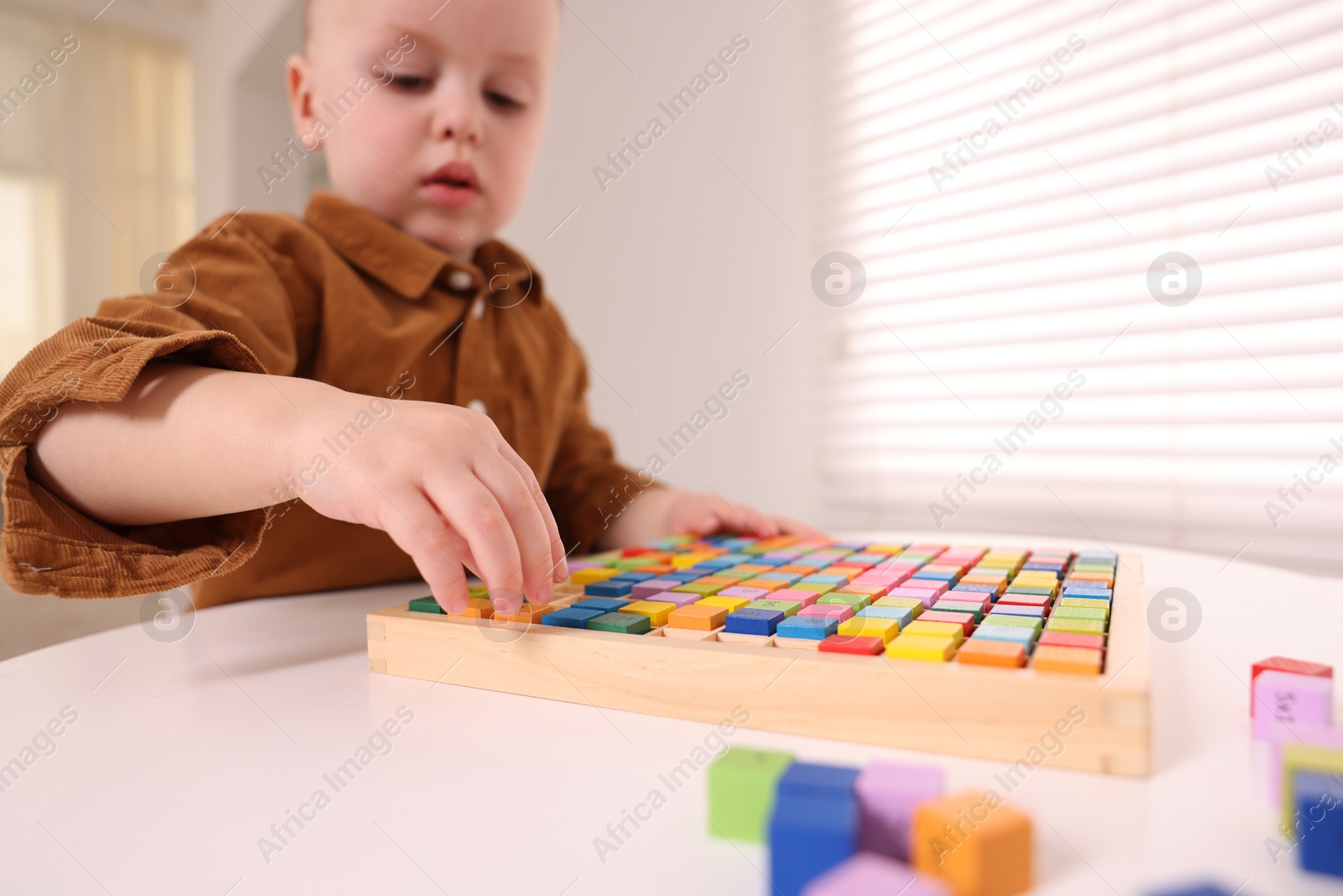 Photo of Motor skills development. Little boy playing with Times table tray indoors, selective focus