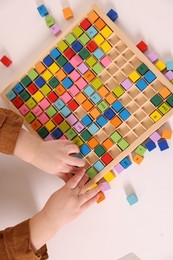 Photo of Motor skills development. Little boy playing with Times table tray at white table, top view