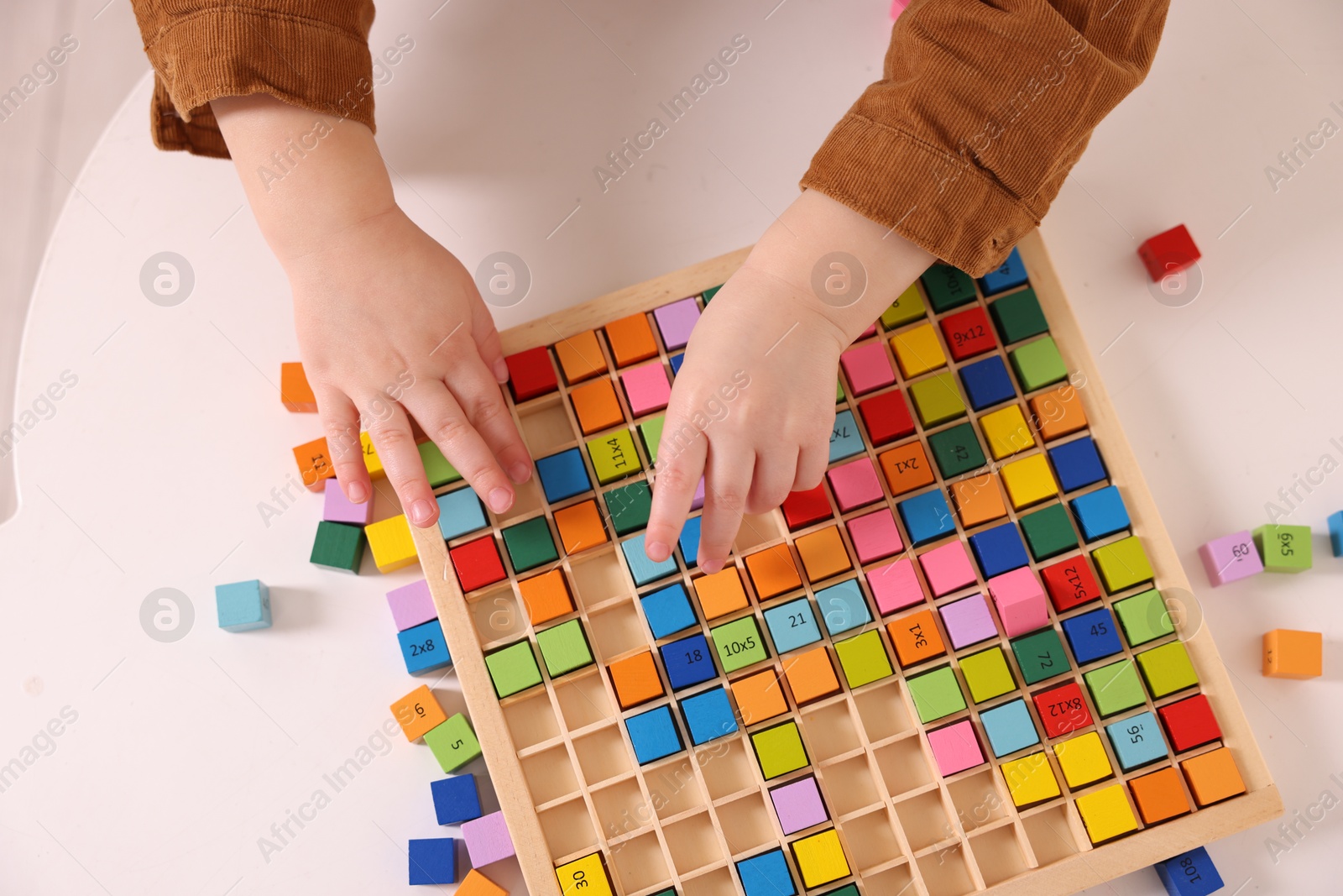 Photo of Motor skills development. Little boy playing with Times table tray at white table, top view