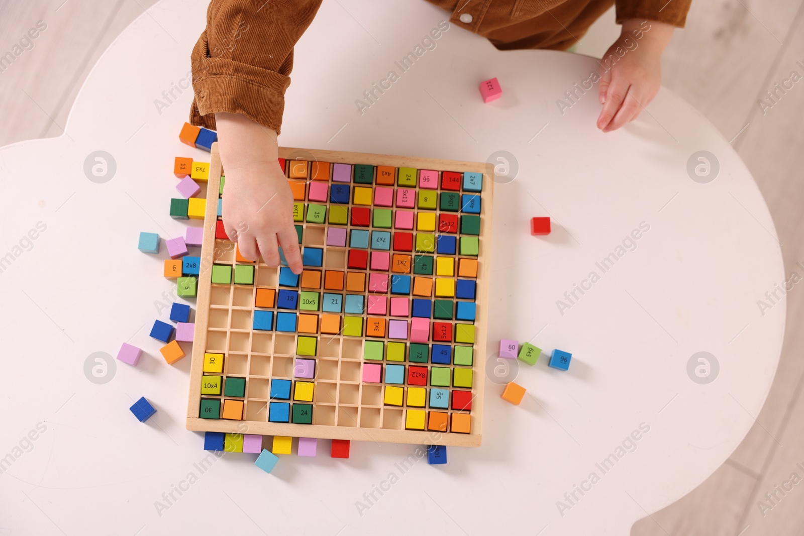 Photo of Motor skills development. Little boy playing with Times table tray at white table, top view