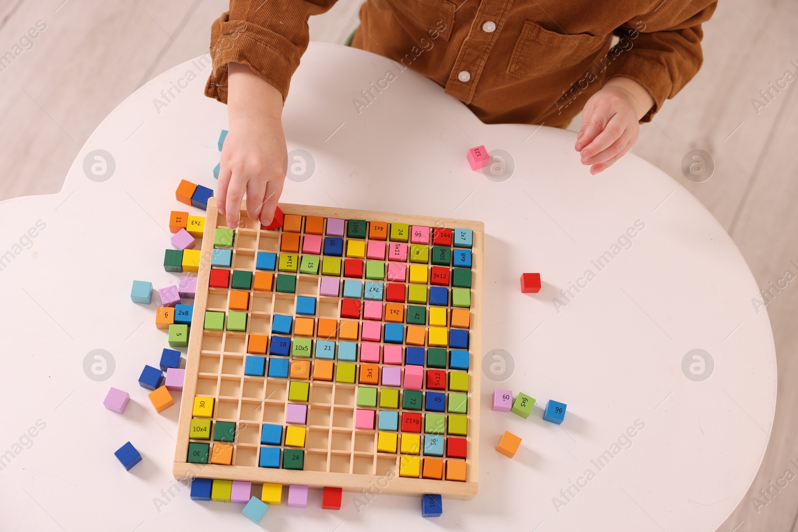 Photo of Motor skills development. Little boy playing with Times table tray at white table, top view