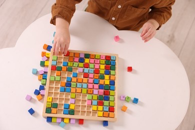 Photo of Motor skills development. Little boy playing with Times table tray at white table, top view