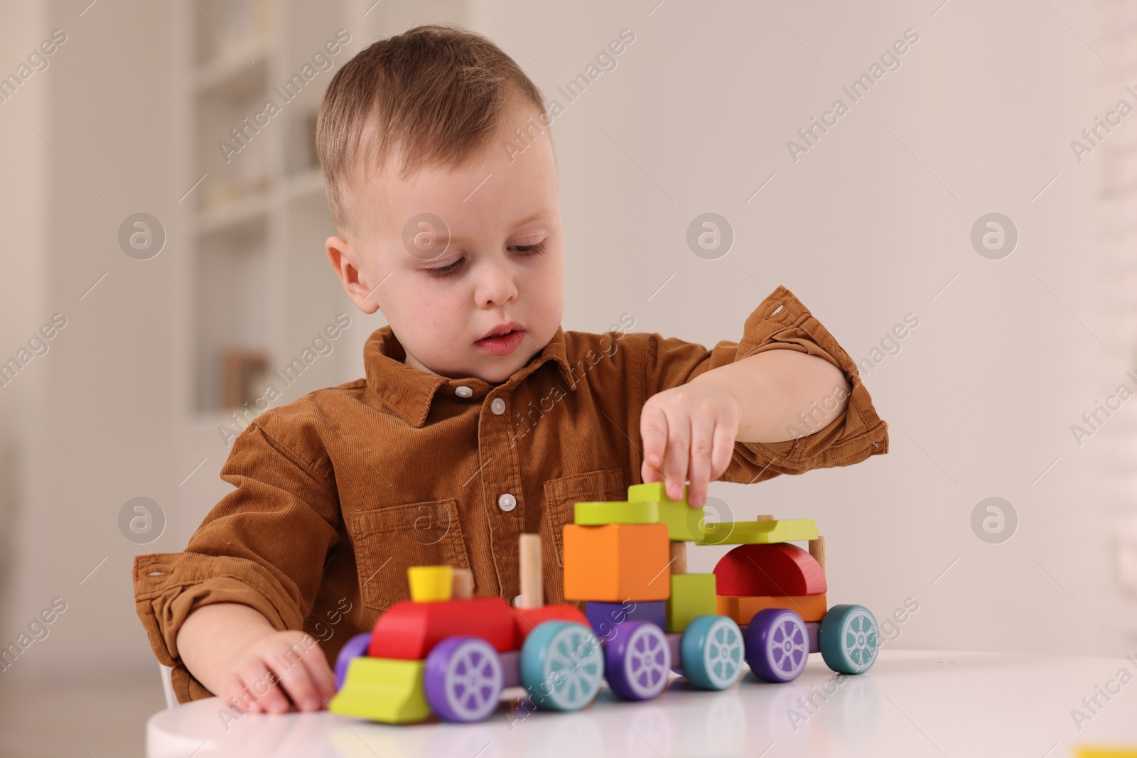 Photo of Motor skills development. Little boy playing with train toy at white table indoors