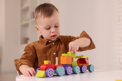 Motor skills development. Little boy playing with train toy at white table indoors