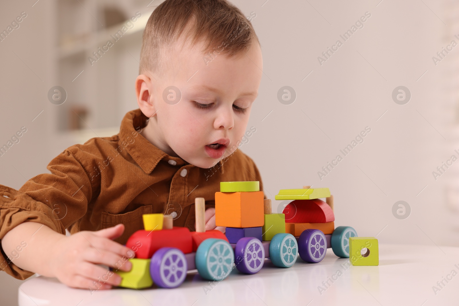 Photo of Motor skills development. Little boy playing with train toy at white table indoors