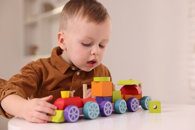 Motor skills development. Little boy playing with train toy at white table indoors