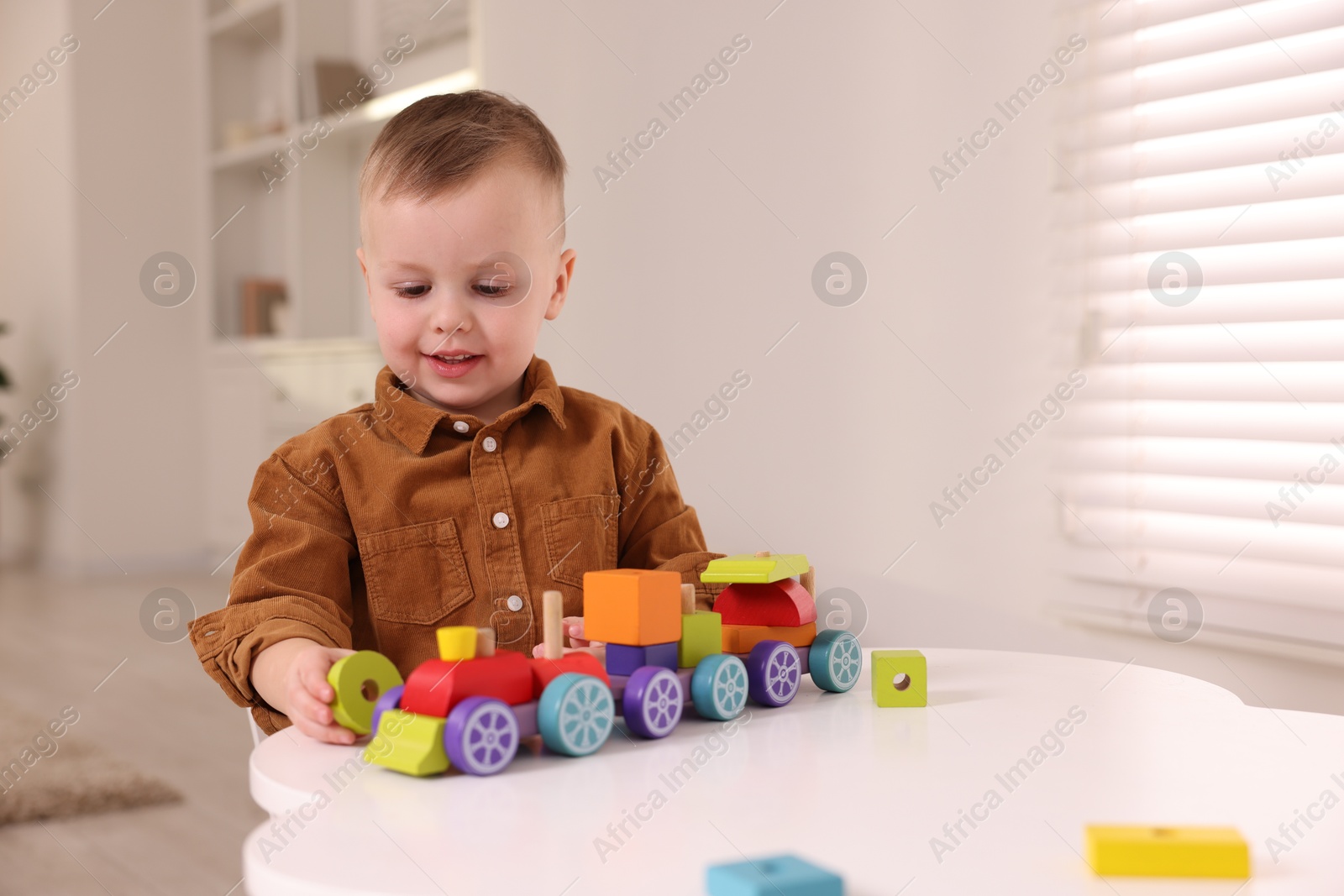 Photo of Motor skills development. Little boy playing with train toy at white table indoors, space for text