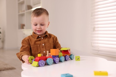 Photo of Motor skills development. Little boy playing with train toy at white table indoors, space for text