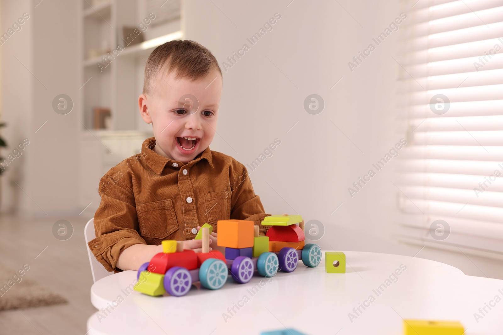 Photo of Motor skills development. Little boy playing with train toy at white table indoors, space for text