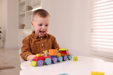 Photo of Motor skills development. Little boy playing with train toy at white table indoors, space for text