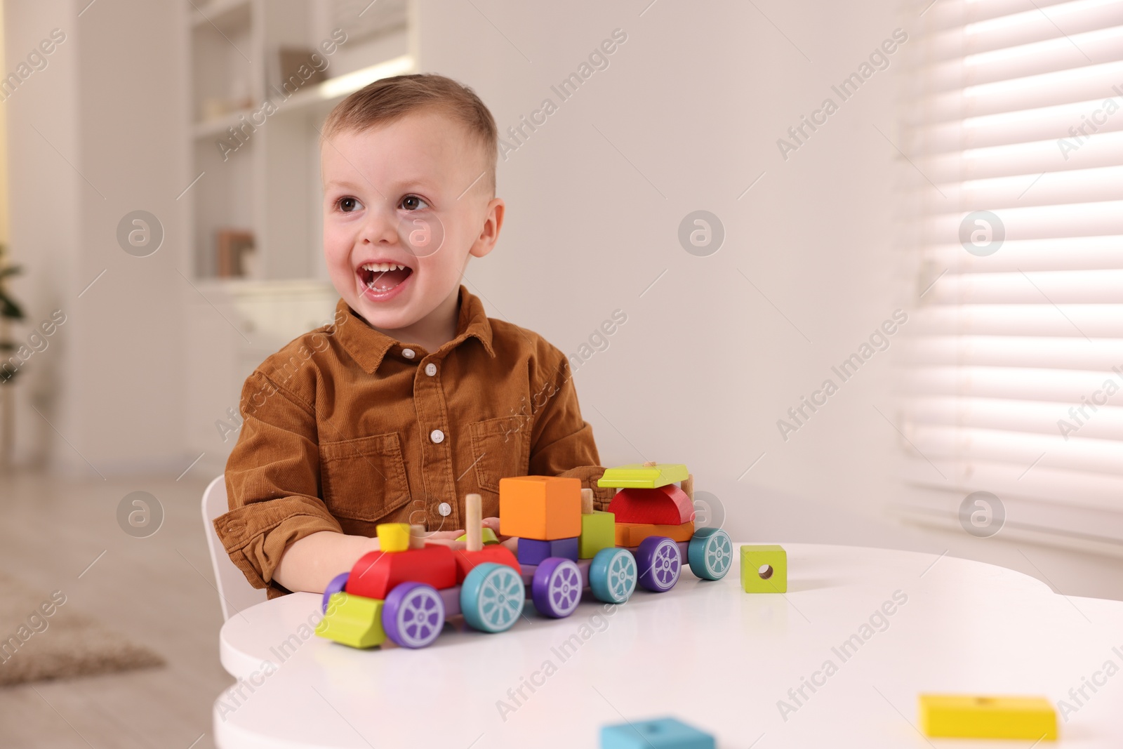 Photo of Motor skills development. Little boy playing with train toy at white table indoors, space for text