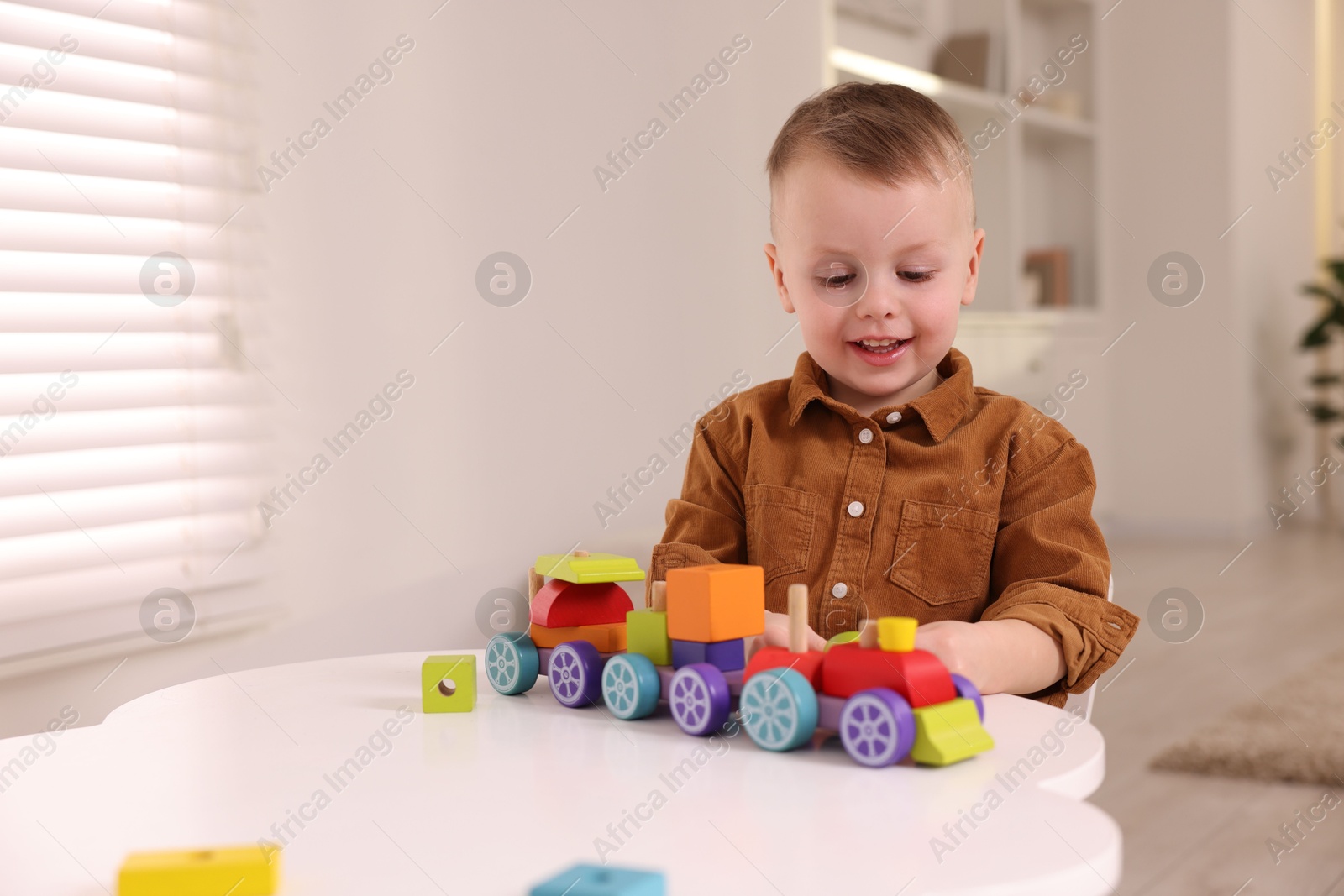 Photo of Motor skills development. Little boy playing with train toy at white table indoors, space for text