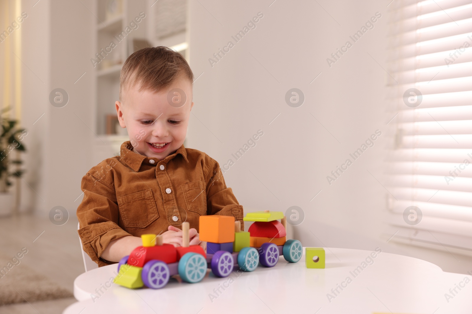 Photo of Motor skills development. Little boy playing with train toy at white table indoors, space for text