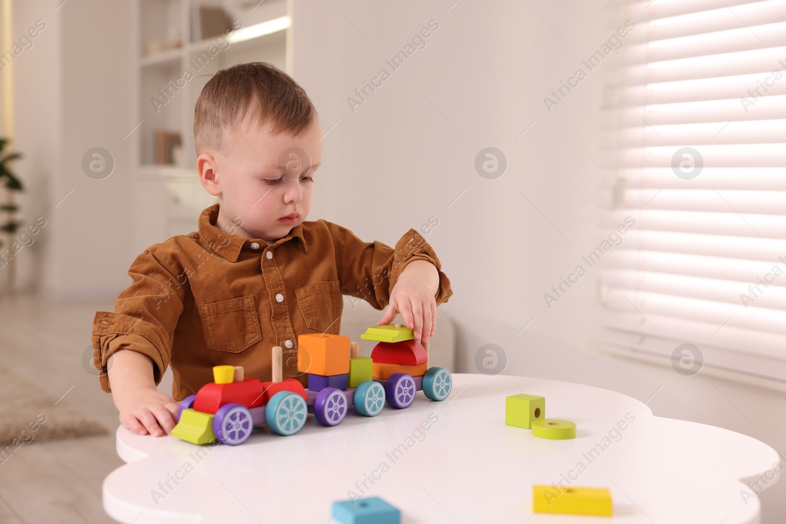 Photo of Motor skills development. Little boy playing with train toy at white table indoors, space for text