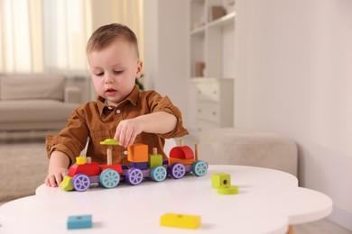 Motor skills development. Little boy playing with train toy at white table indoors, space for text