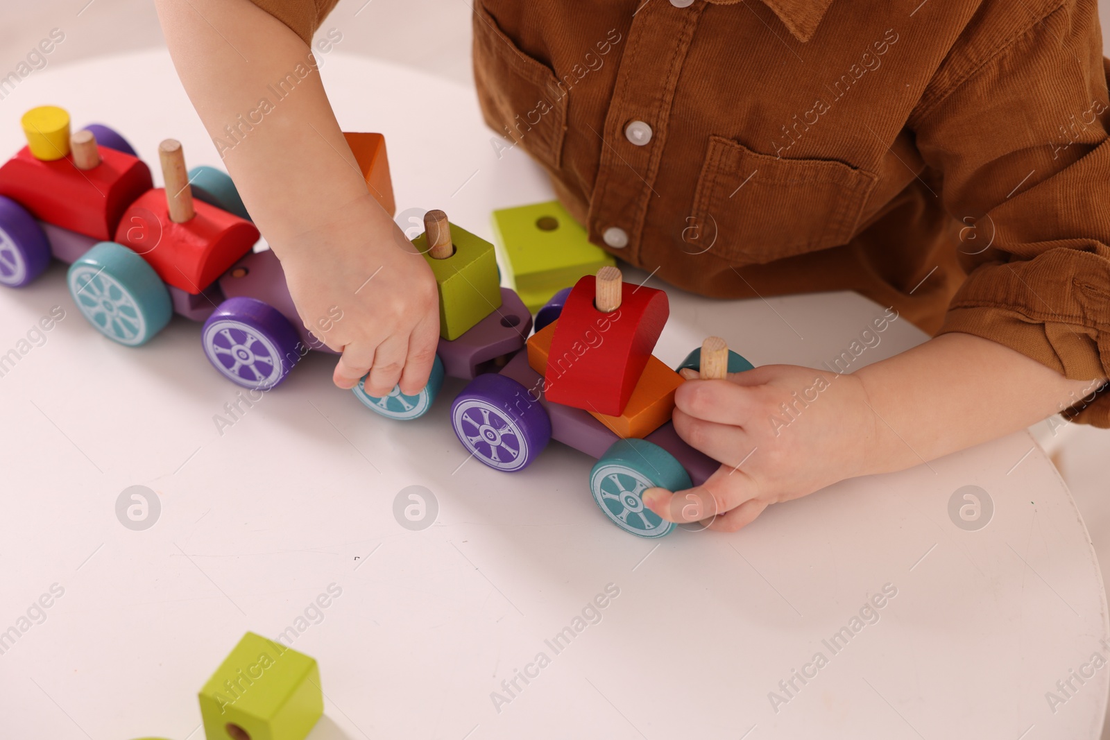 Photo of Motor skills development. Little boy playing with train toy at white table indoors, closeup