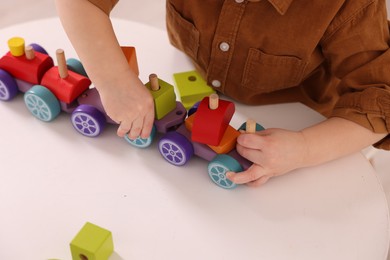 Motor skills development. Little boy playing with train toy at white table indoors, closeup