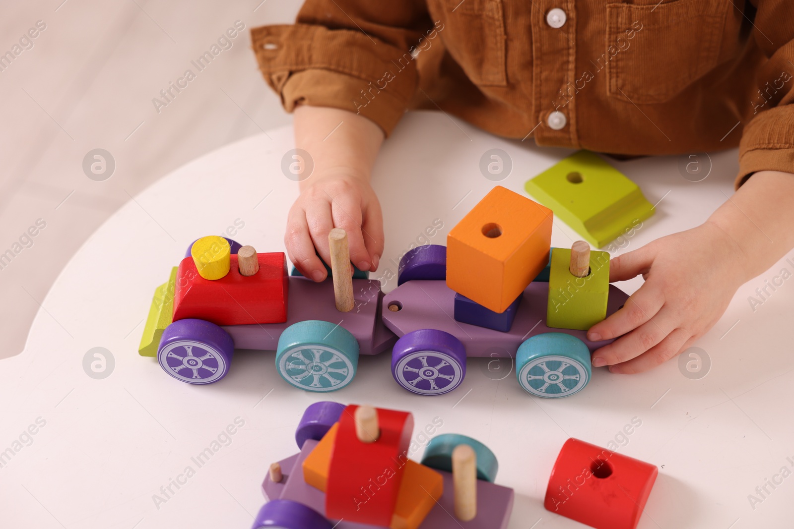 Photo of Motor skills development. Little boy playing with train toy at white table indoors, closeup