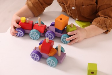 Photo of Motor skills development. Little boy playing with train toy at white table indoors, closeup