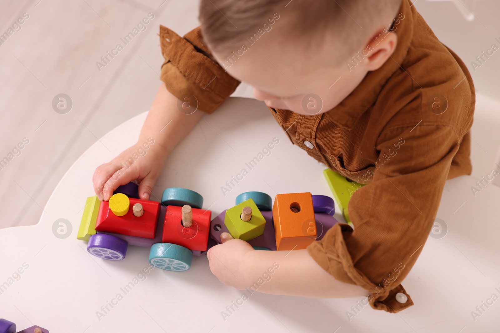 Photo of Motor skills development. Little boy playing with train toy at white table indoors, above view