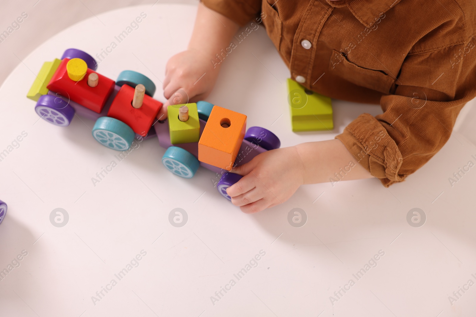 Photo of Motor skills development. Little boy playing with train toy at white table indoors, above view