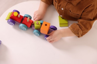 Motor skills development. Little boy playing with train toy at white table indoors, above view