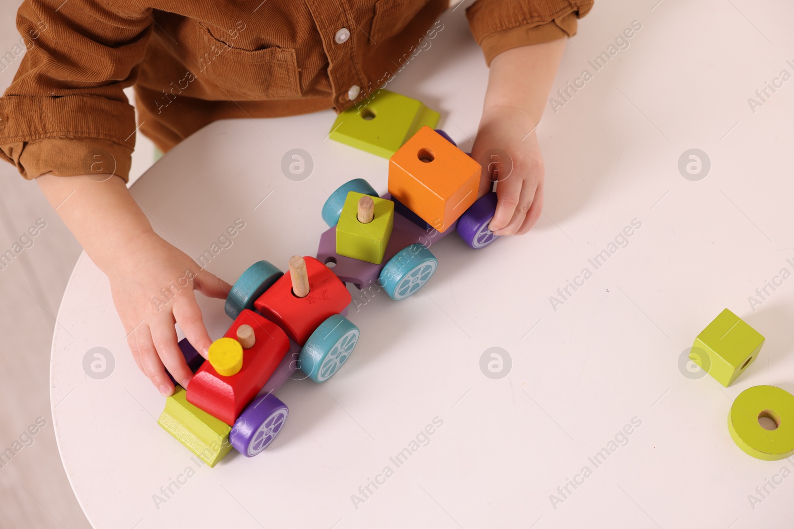 Photo of Motor skills development. Little boy playing with train toy at white table indoors, above view