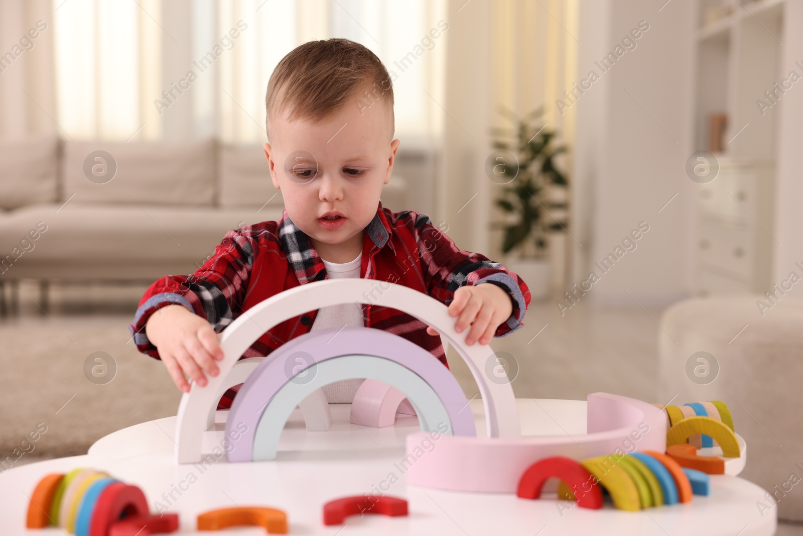 Photo of Motor skills development. Little boy playing with toys at white table indoors