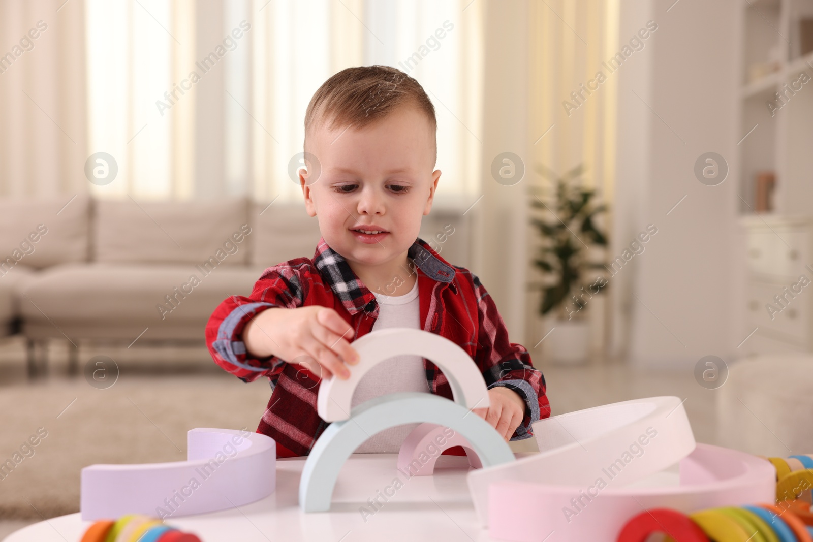 Photo of Motor skills development. Little boy playing with toys at white table indoors