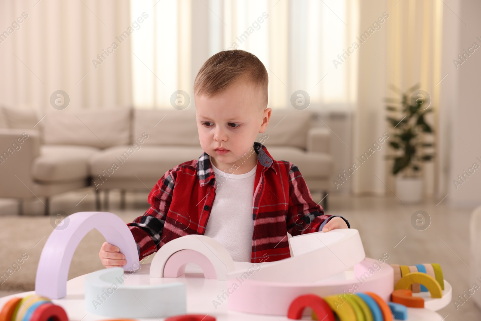 Photo of Motor skills development. Little boy playing with toys at white table indoors