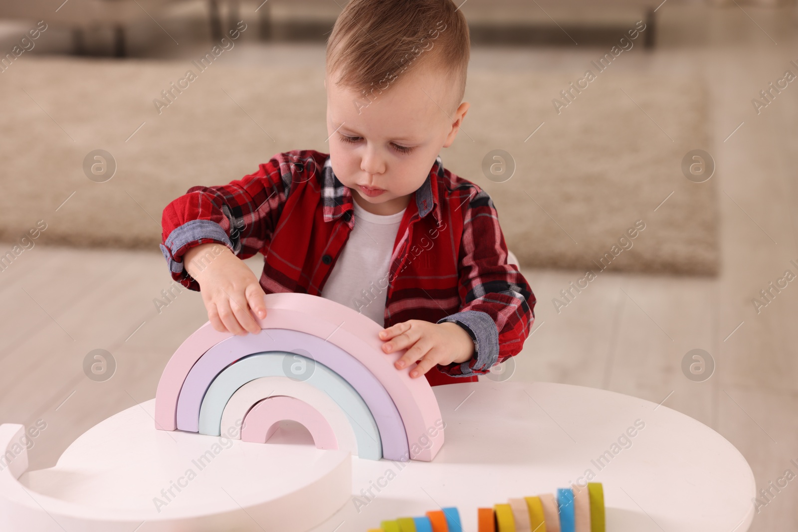 Photo of Motor skills development. Little boy playing with toys at white table indoors